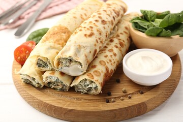 Tasty rolled crepes with cottage cheese and spinach served on white wooden table, closeup