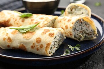 Delicious crepes with cottage cheese and spinach on black table, closeup