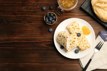 Delicious crepes with cottage cheese, jam and blueberries served on wooden table, flat lay. Space for text