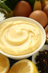 Delicious mayonnaise sauce in bowl and ingredients on table, closeup