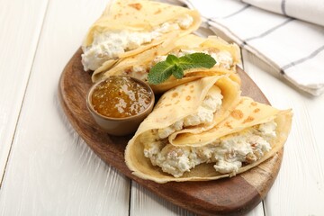 Delicious crepes with cottage cheese, jam and mint on white wooden table, closeup