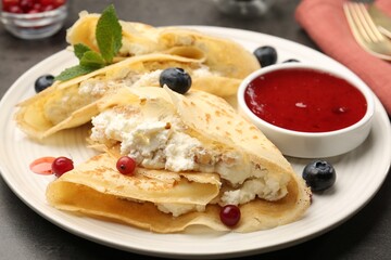 Delicious crepes with cottage cheese, jam, redcurrants and blueberries on grey table, closeup