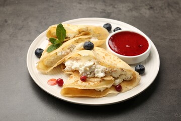 Delicious crepes with cottage cheese, jam, redcurrants and blueberries on grey table, closeup