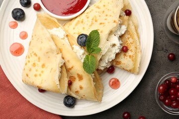 Delicious crepes with cottage cheese, jam, redcurrants and blueberries on grey table, flat lay