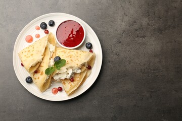 Delicious crepes with cottage cheese, jam, redcurrants and blueberries on grey table, top view. Space for text
