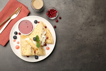 Delicious crepes with cottage cheese, jam, redcurrants and blueberries served on grey table, flat lay. Space for text