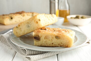 Pieces of delicious focaccia bread with olives, thyme and salt on white wooden table, closeup