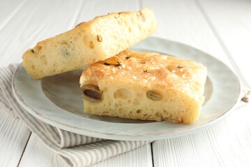 Pieces of delicious focaccia bread with olives, thyme and salt on white wooden table, closeup