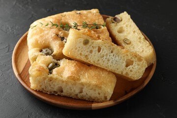 Slices of delicious focaccia bread with olives, thyme and salt on black table, closeup