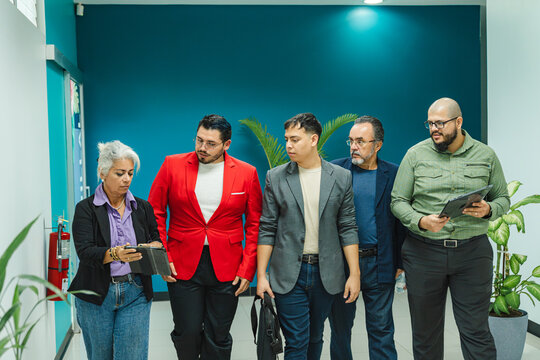 A diverse group of professionals walks while reviewing information on a tablet in a modern environment.