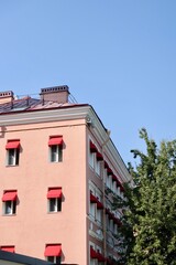 classic-style historic pink house with red awnings on windows. sunny day. stylish architecture in center of metropolis. hotel or apartment building