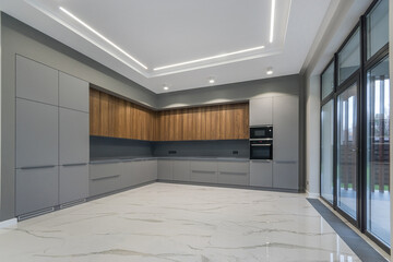 A kitchen with a built-in gray kitchen set in a luxurious country house. White tiled floor, .panoramic window. Unfurnished.
