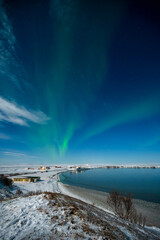 Aurora Borealis or Northern lights the amazing wonder of nature in the dramatic skies of Iceland. Night landscape with the green light and the white snow of winter