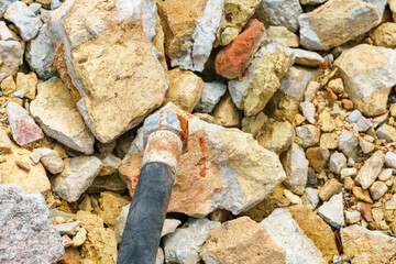 An old rubber hose for the hydraulic system drive against a background of stones and broken bricks.