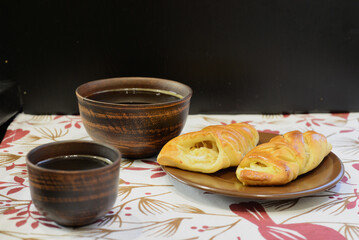 Two rustic brown clay cups of coffee and two pastries with a white filling on a plate. The dark brown background makes the food look warm and inviting