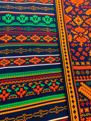 Colorful traditional fabric with intricate patterns and black, green, orange, and yellow colors.