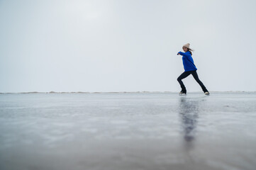 Caucasian woman in a blue sweater is skating on a frozen lake. The figure skater performs the program.