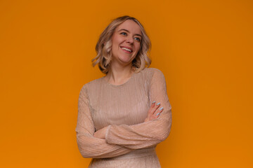 Blonde woman in a sparkling gold dress stands confidently against a vibrant orange background, smiling warmly with arms crossed. Perfect for themes of elegance, confidence, and fashion. © My Ocean studio