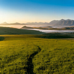広大な緑の草原が広がる風景を描いています。遠くには山々と霧が立ち込めた谷があり、朝の澄んだ青空が全体を包み込んでいます。自然の穏やかさと美しさを象徴する情景です。