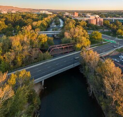 Aerial view of a city street, bridge, and river. Cars travel on the road beneath the bridge. Autumn...