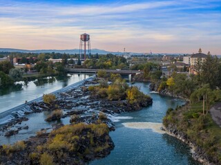 Aerial view of the Snake River, a dam, and the city. Tranquil morning light illuminates the water and surrounding landscape. Snake River, Idaho Falls, Idaho, USA.