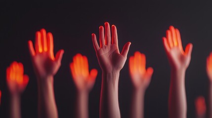 Fototapeta premium A group of raised hands illuminated with a red glow against a dark background, symbolizing unity, support, or a call to action.