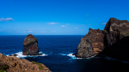 Fototapeta premium Majestic rocky cliffs and a sea stack rising from the deep blue ocean under a clear sky. The dramatic coastal scenery highlights the beauty of nature.