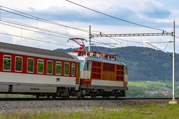 Obraz premium A passenger train on an electrified track passing through the countryside.