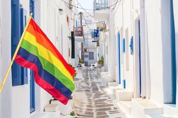 Mykonos old town cozy narrow street with Rainbow flag LGBT movement symbol, white houses and blue windows on Mykonos island, Greece