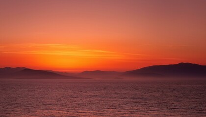 Fiery sunset over calm ocean and distant mountains. A breathtaking view of nature's beauty.