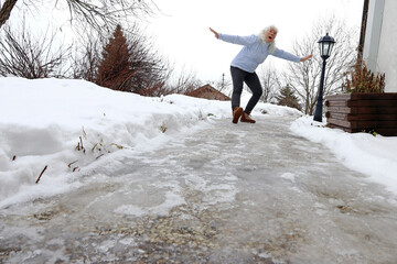 Rutschgefahr auf einem eisglatten Gehweg im Winter. Eine Frau rutscht auf Glatteis aus
