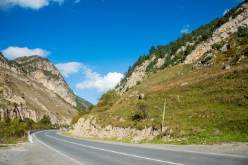 automobile road in the middle of the mountains and going further into the mountains against the background of blue sky with clouds
