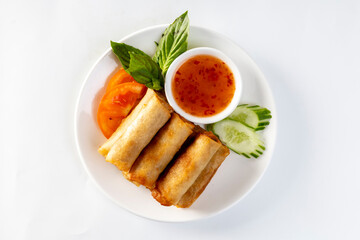 Fried spring rolls, vegetables  with dipping sauce on a white background.