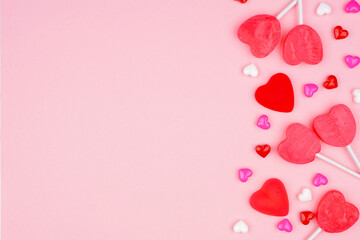 Valentines Day side border of candy hearts and lollipops. Overhead view on a pink background. Copy space.