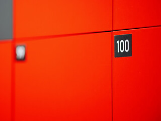 Cabinet with cells for storing buyer things at entrance to shopping center. Orange safe locker cabinet with keys and black number plate 100. December 31, 2024 - Pula, Croatia
