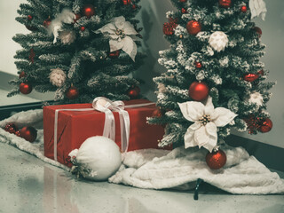 Red gift box tied with white satin ribbon. Present under tree. Christmas tree decorations on branches of Artificial Christmas tree. New Year celebration concept. December 31, 2024 - Pula, Croatia