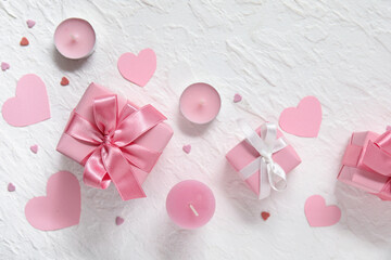 Fototapeta premium Pink gift boxes, paper hearts and candles on white grunge background. Valentine's Day celebration