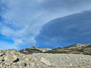 A dark cloud in the abstract shape of the side profile of a person above an area of large jumbled rocks.