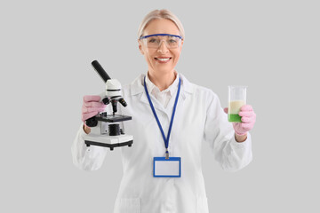 Female chemist with microscope and flask on light background