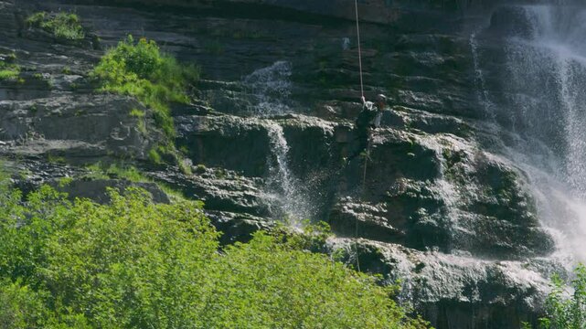 Man rappelling down cliff and running across cliffside wall to waterfall in majestic slow motion