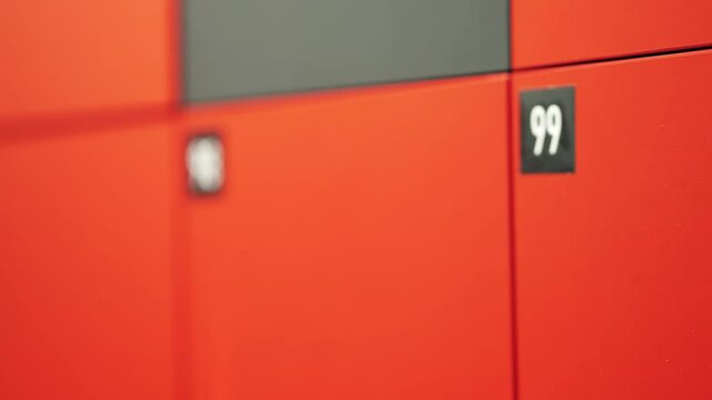 Cabinet with cells for storing buyer things at entrance to shopping center. Orange safe locker cabinet with keys and black number plates 99 and 100. December 31, 2024 - Pula, Croatia