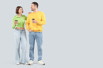 Young couple in jeans with coffee cups on light background