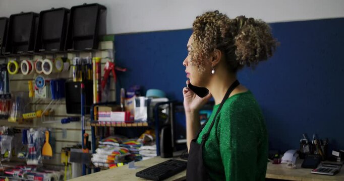 Dedicated shopkeeper on a phone call at the counter in a hardware store, surrounded by tools and supplies, managing tasks with professionalism and focus