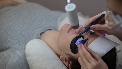 A woman undergoing eyelash extension procedure using an ultraviolet lamp.