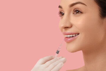 Beautiful young happy woman receiving lips injection on pink background