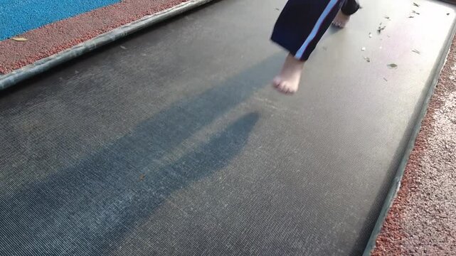 Barefoot child walking on a black trampoline. Perfect for projects related to childhood, fun, and outdoor activities. High-quality footage.