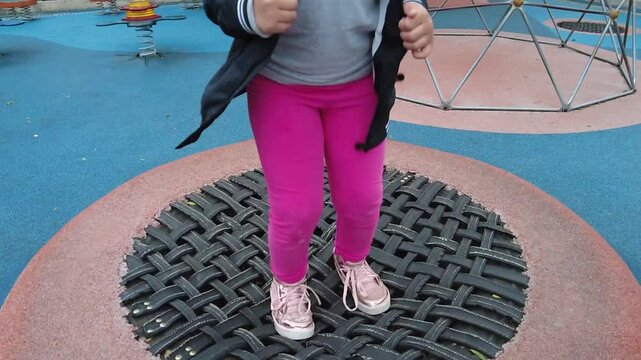 Girl playing in the park and jumping on recycled tire mini trampoline.