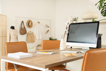 Workplace with blank computer monitor and cotton flowers in clothing store office