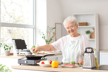 Senior woman putting cut bell pepper into frying pan in kitchen