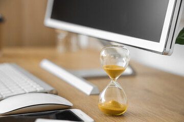 Hourglass and computer on desk in office, closeup